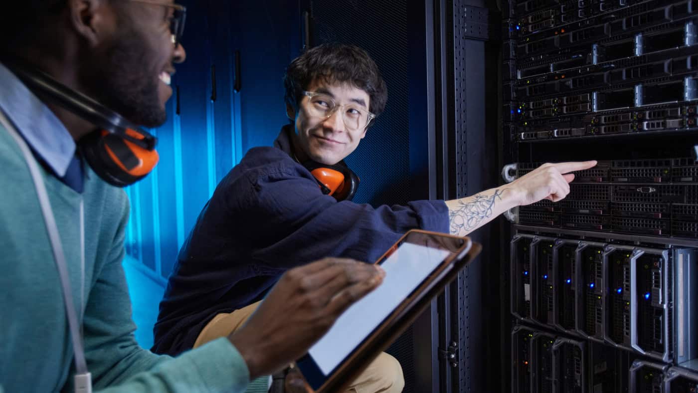 Man pointing to server in a data center with another man looking on.