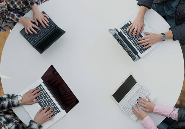 Overhead view of 4 people at a round table all with hands on keyboards of laptop computers